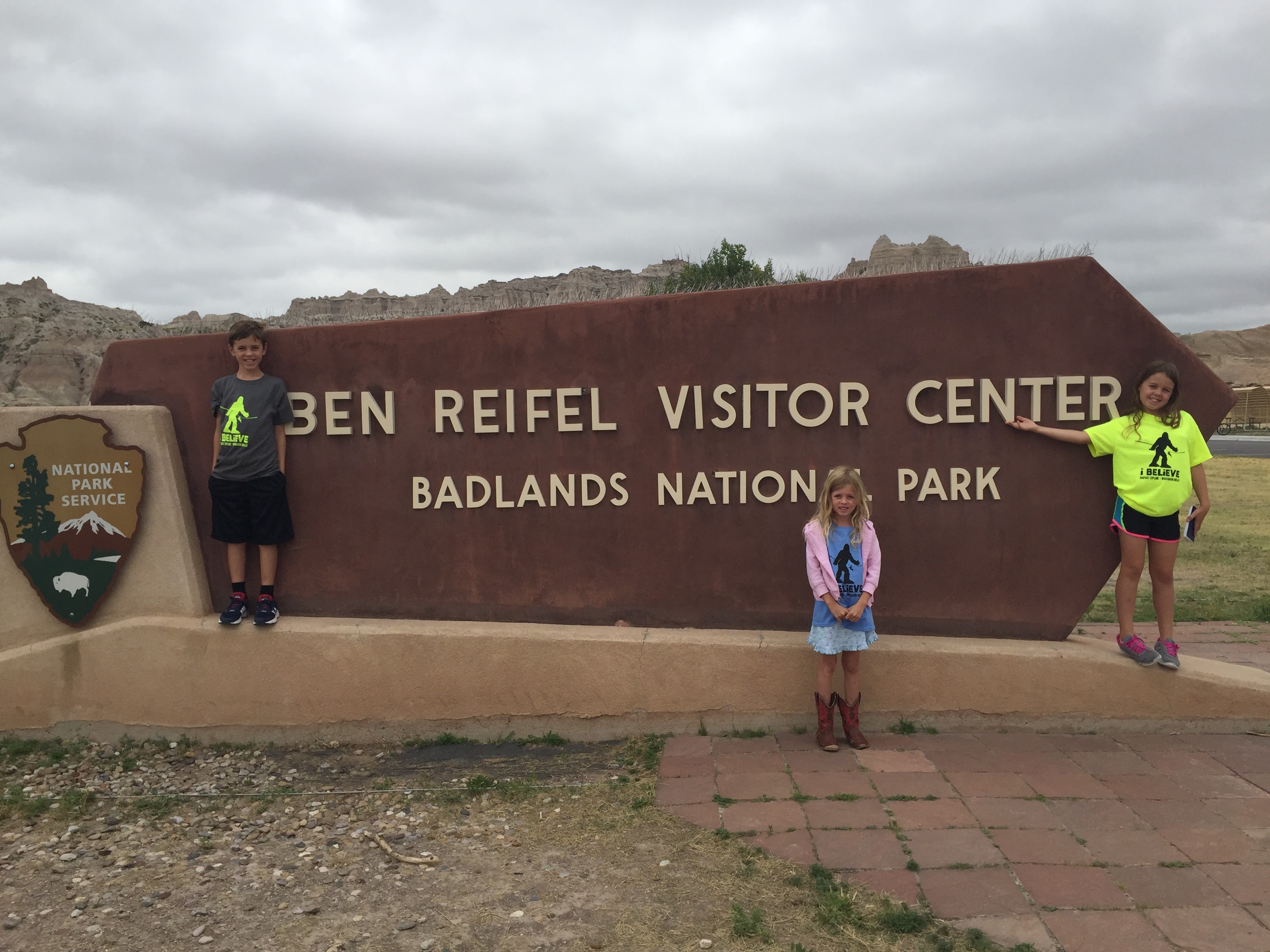 A boy and two girls standing seperately in front of sign for Badlands National Park