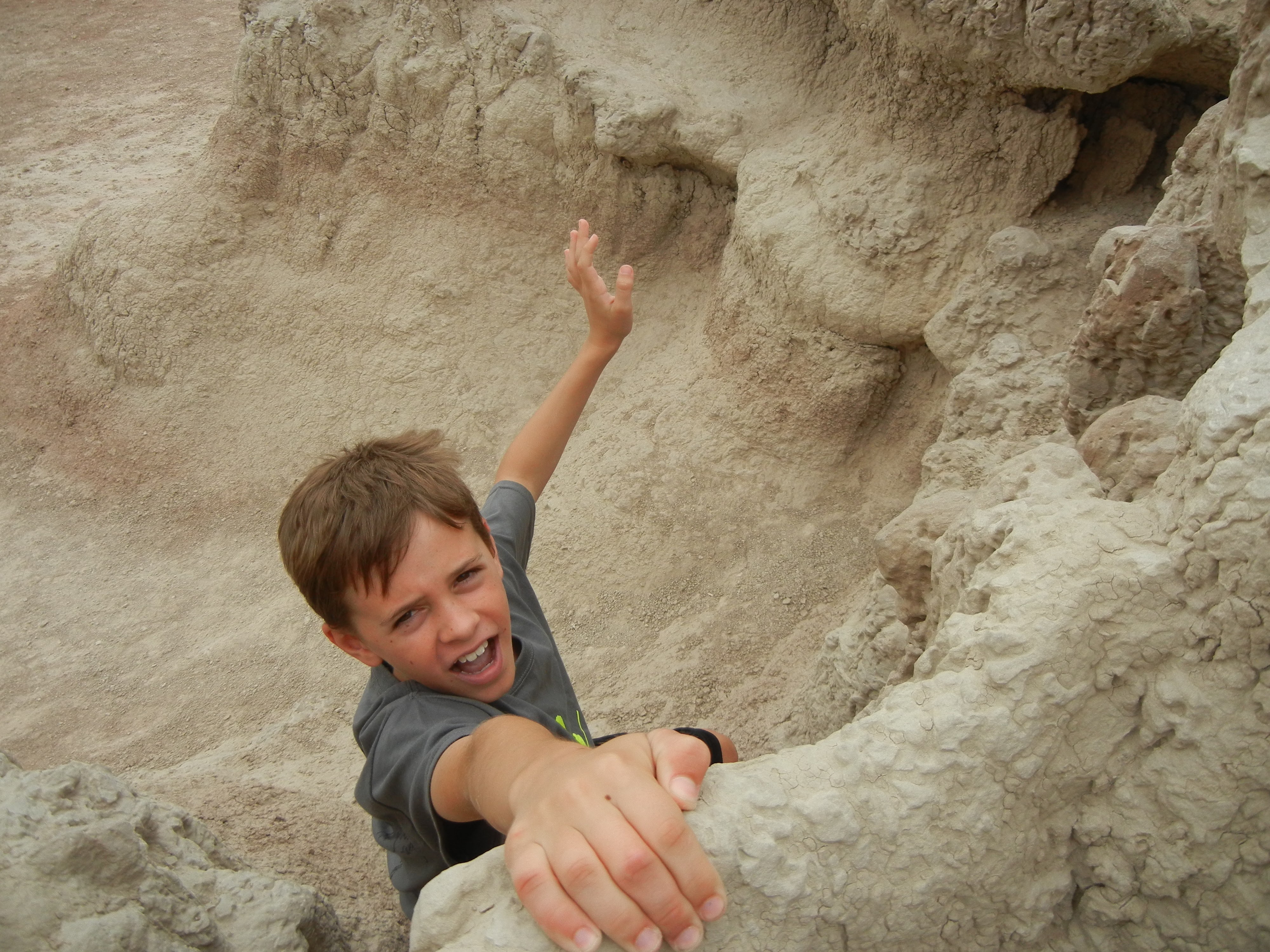 A boy about to fell off a low cliff while one hand holding its border